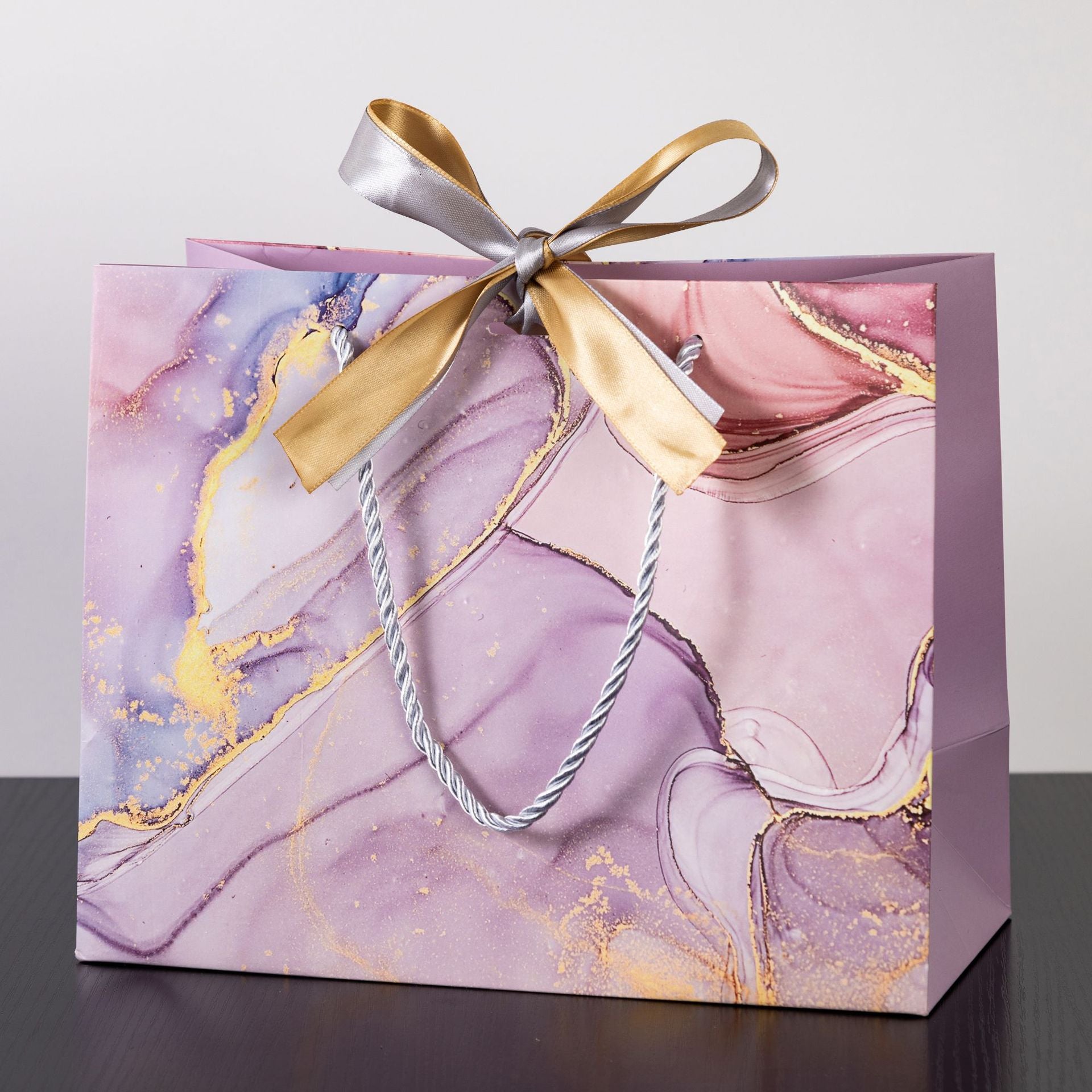 Pink marble gift bag with gold accents, braided handles, and a dual-tone ribbon bow for romantic occasions.