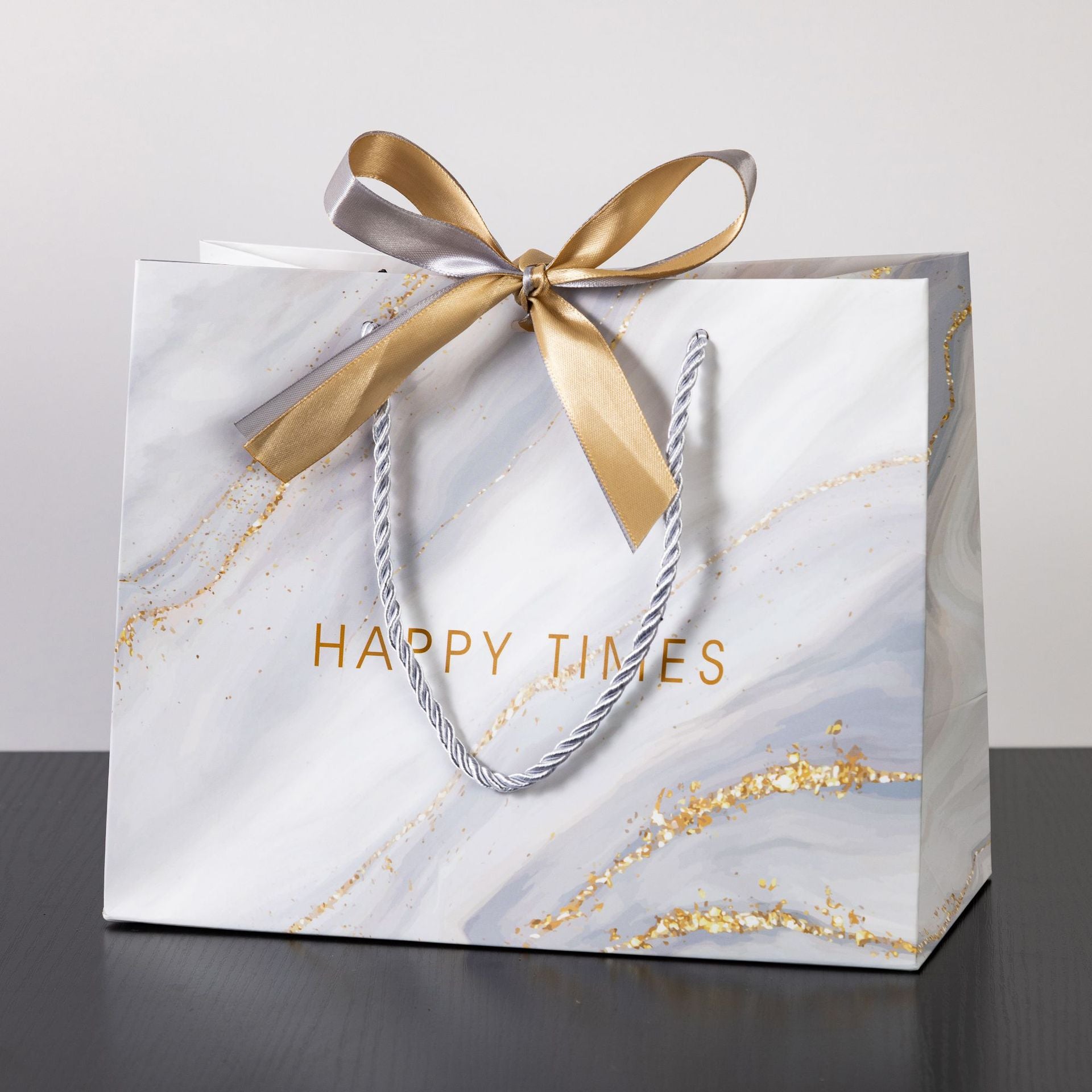 White marble gift bag with gold accents, braided handles, and ribbon bow featuring 'HAPPY TIMES' text.